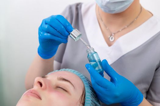 Hands of cosmetologist dripping nourishing oil facial skin of young woman in spa salon. Facial treatment and skincare concept.