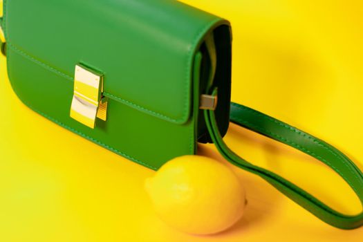 stylish little green purse or handbag on yellow background with a lemon nearby. Product composition photography. bag and reticule for women.