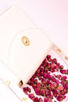 fashion photo of purse. white woman handbag near little roses flowers. isolated on white and pink background. Product composition photography.