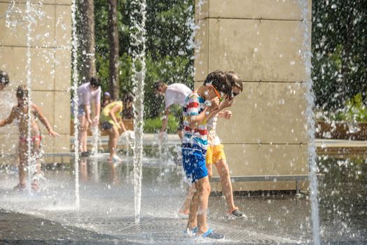 Kyiv, Ukraine - August 01, 2021: Boys jumping in water fountains. Children playing with a city fountain on hot summer day. Happy friends having fun in fountain. Summer weather. Friendship, lifestyle and vacation.