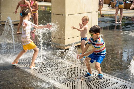 Kyiv, Ukraine - August 01, 2021: Boys jumping in water fountains. Children playing with a city fountain on hot summer day. Happy friends having fun in fountain. Summer weather. Friendship, lifestyle and vacation.