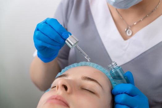 Hands of cosmetologist dripping nourishing oil facial skin of young woman in spa salon. Facial treatment and skincare concept.