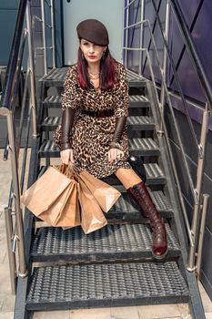 A happy shopaholic girl keeps her bags near the shopping center. A woman near the store is happy with her purchases, holding bags. Dressed in a leopard print dress. Consumer concept