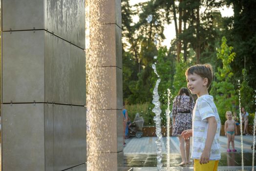 Kyiv, Ukraine - August 01, 2021: Boys jumping in water fountains. Children playing with a city fountain on hot summer day. Happy friends having fun in fountain. Summer weather. Friendship, lifestyle and vacation.