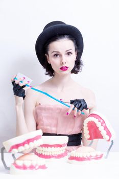 A woman in a dress and hat sits at a table and holds a mock-up of her teeth. High quality photo