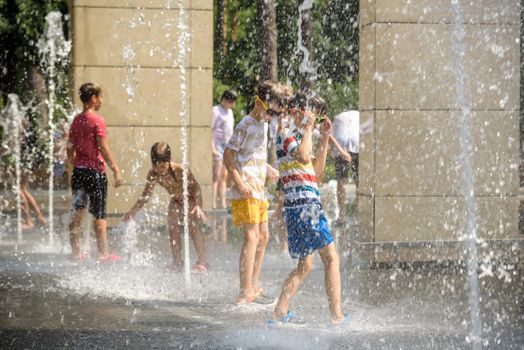 Kyiv, Ukraine - August 01, 2021: Boys jumping in water fountains. Children playing with a city fountain on hot summer day. Happy friends having fun in fountain. Summer weather. Friendship, lifestyle and vacation.