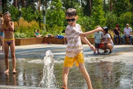 Kyiv, Ukraine - August 01, 2021: Boys jumping in water fountains. Children playing with a city fountain on hot summer day. Happy friends having fun in fountain. Summer weather. Friendship, lifestyle and vacation.