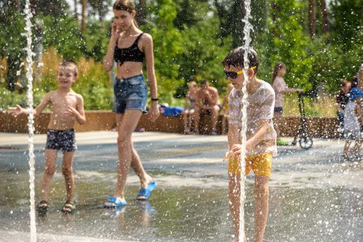 Kyiv, Ukraine - August 01, 2021: Boys jumping in water fountains. Children playing with a city fountain on hot summer day. Happy friends having fun in fountain. Summer weather. Friendship, lifestyle and vacation.