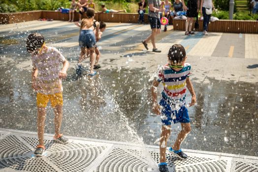 Kyiv, Ukraine - August 01, 2021: Boys jumping in water fountains. Children playing with a city fountain on hot summer day. Happy friends having fun in fountain. Summer weather. Friendship, lifestyle and vacation.