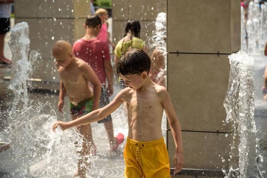 Kyiv, Ukraine - August 01, 2021: Boys jumping in water fountains. Children playing with a city fountain on hot summer day. Happy friends having fun in fountain. Summer weather. Friendship, lifestyle and vacation.