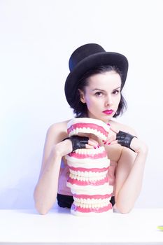 A woman in a dress and hat sits at a table and holds a mock-up of her teeth. High quality photo