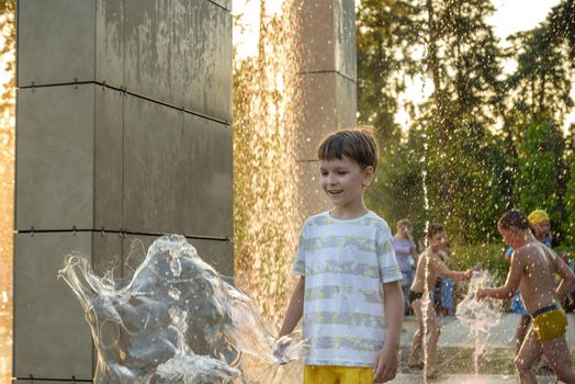 Kyiv, Ukraine - August 01, 2021: Boys jumping in water fountains. Children playing with a city fountain on hot summer day. Happy friends having fun in fountain. Summer weather. Friendship, lifestyle and vacation.