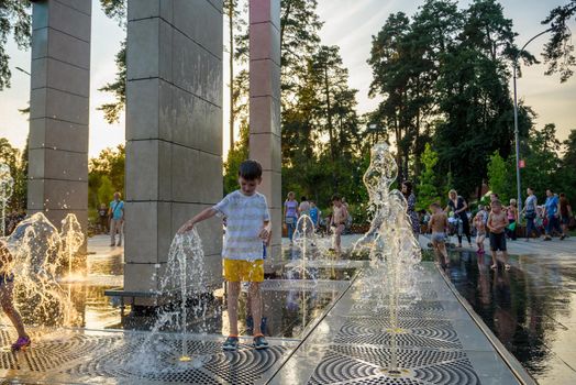 Kyiv, Ukraine - August 01, 2021: Boys jumping in water fountains. Children playing with a city fountain on hot summer day. Happy friends having fun in fountain. Summer weather. Friendship, lifestyle and vacation.