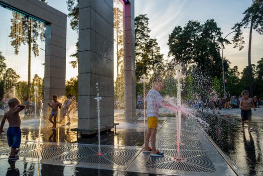 Kyiv, Ukraine - August 01, 2021: Boys jumping in water fountains. Children playing with a city fountain on hot summer day. Happy friends having fun in fountain. Summer weather. Friendship, lifestyle and vacation.