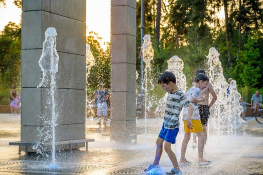 Kyiv, Ukraine - August 01, 2021: Boys jumping in water fountains. Children playing with a city fountain on hot summer day. Happy friends having fun in fountain. Summer weather. Friendship, lifestyle and vacation.