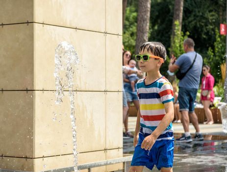 Kyiv, Ukraine - August 01, 2021: Boys jumping in water fountains. Children playing with a city fountain on hot summer day. Happy friends having fun in fountain. Summer weather. Friendship, lifestyle and vacation.