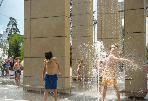 Kyiv, Ukraine - August 01, 2021: Boys jumping in water fountains. Children playing with a city fountain on hot summer day. Happy friends having fun in fountain. Summer weather. Friendship, lifestyle and vacation.