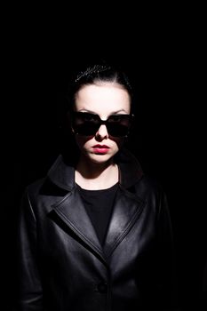 woman in leather coat and black sunglasses, black background. High quality photo