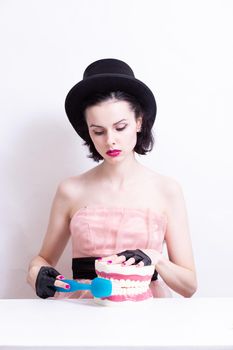 A woman in a dress and hat sits at a table and holds a mock-up of her teeth. High quality photo