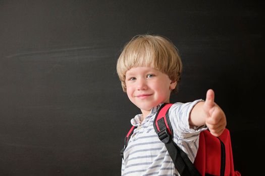 Back to school. Funny little boy at blackboard. Child from elementary school with book and bag. Education concept.