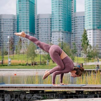 Young woman doing yoga exercises with city on background. eka pada kaundiniasana, balance pose