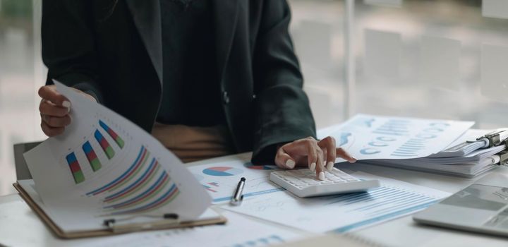 Close up of businesswoman or accountant hand holding pen working on calculator to calculate business data, accountancy document and laptop computer at office, business concept.