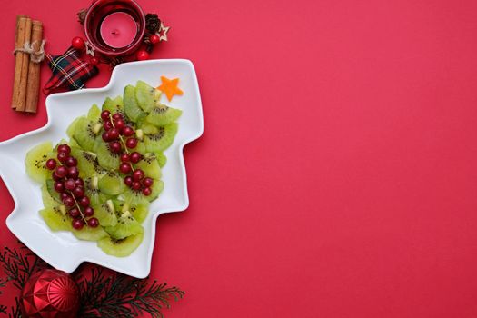 Creative edible vegan christmas tree, food art. Food for kids and festive table. Tree made from kiwi on a white tree plate
