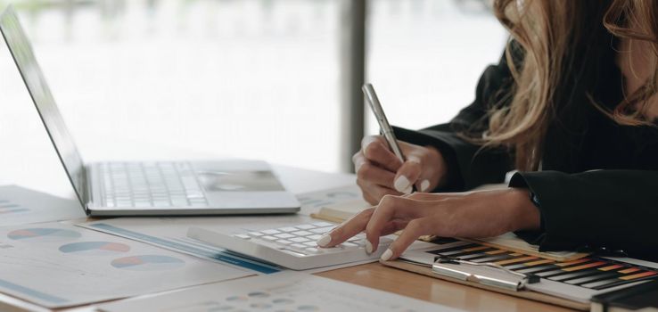 Close up of businesswoman or accountant hand holding pen working on calculator to calculate business data, accountancy document and laptop computer at office, business concept.