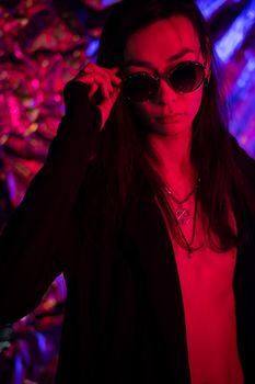 Portrait of a transgender model in sunglasses in a studio with neon lighting