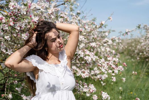 Spring concept. Nature.Young caucasian woman enjoying the flowering of an apple trees, walking in spring apple gardens. Shadow overlay on face