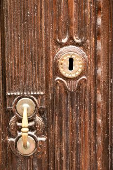 Golden doorknocker with modernist style on old brown wooden door in Villajoyosa, Alicante, Spain