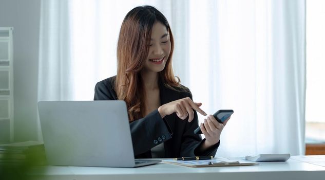 Portrait of young asian business woman used smartphone write notebook laptop in home office. Beautiful girl at desk computer take home order. Startup business asia woman online sme telemarketing..