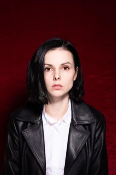 Woman in white shirt and black leather jacket on red velvet background. High quality photo