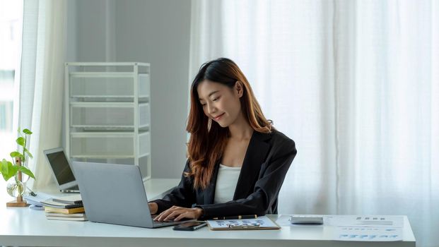 Charming asian businesswoman sitting working on laptop in office.