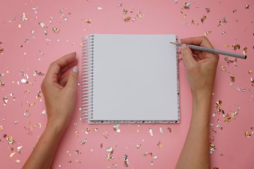 Blank notebook and female hands with pencil on festive pink background, view from above