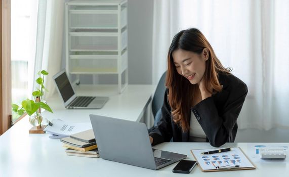 Happy young asian businesswoman sitting on her workplace in the office. Young woman working at laptop in the office..