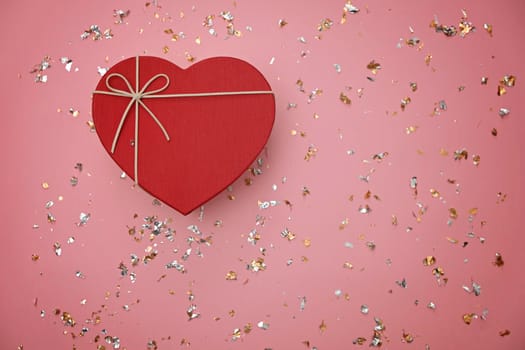 Red heart shape gift box on festive pink background, view from above