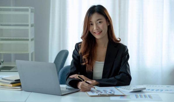 Charming Asian woman working at the office using a laptop Looking at the camera..