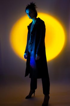 a woman in a black leather coat, in high-heeled shoes illuminated by colored light. High quality photo