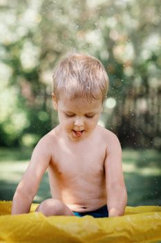 Baby boy concentrated plays at pool in the garden. Showing his tongue. Green nature background. Summer time joys