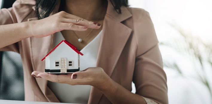 Close up of businesswoman holding model house. Architecture, building, construction, real estate and property concept.