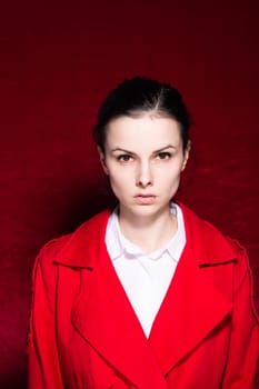 brunette woman in a white shirt red trench on a red background. High quality photo