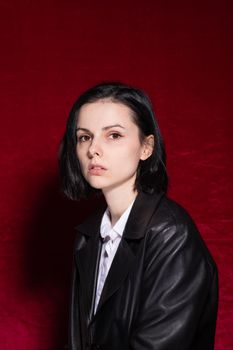 Woman in white shirt and black leather jacket on red velvet background. High quality photo