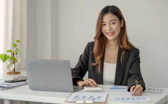 Charming Asian woman working at the office using a laptop Looking at the camera..