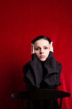 a woman in a black sweater sits at a chair, red background. High quality photo