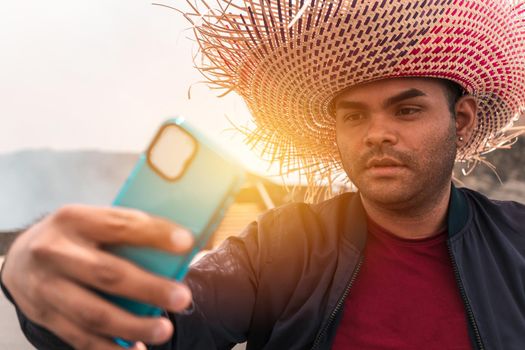 Portrait of a Latin man taking a selfie with his cell phone and wearing a colorful travel hat in an exotic tourist destination in Masaya, Nicaragua.