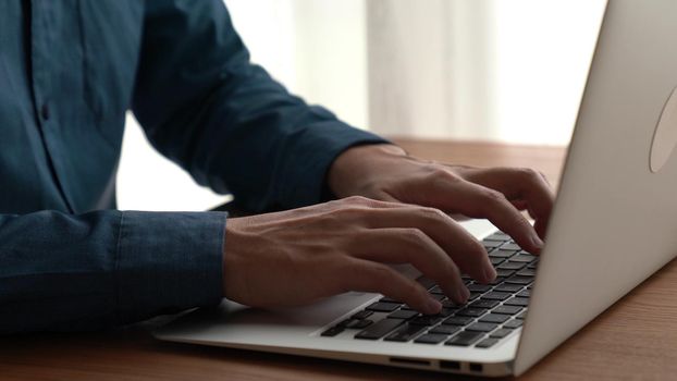 Businessman hand work on capable laptop computer at office table close up shot and selective focus at middle section of laptop computer keyboard while typing and working