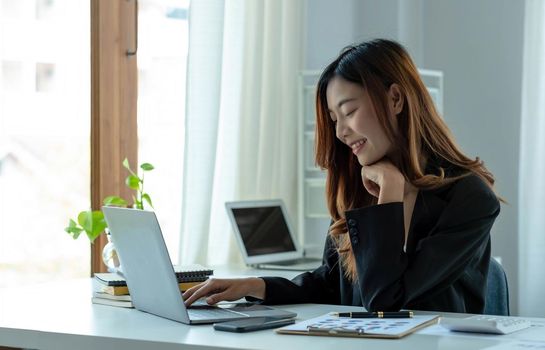 Happy young asian businesswoman sitting on her workplace in the office. Young woman working at laptop in the office..