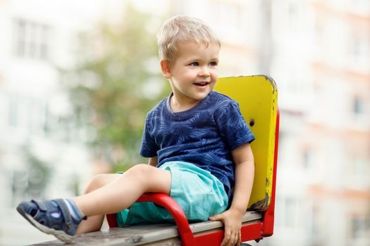 A child is happy to sit on a child’s swing chair in a public playground. He looks into the distance and likes to be raised.