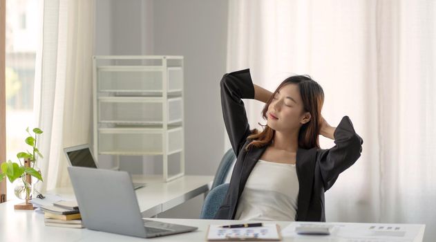 Young Asian businesswoman stretching arms raised relaxing at the office..